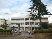 正門の右横に大きな木が生えている3階建ての白い外観の安田中学校の写真