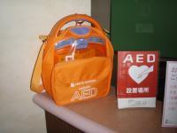 AED機器が入っているオレンジ色のバックとAEDと書かれたアクリルフレームの写真