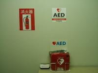 壁に貼ってある消化器とAEDのステッカー、通路に設置されたAEDの写真