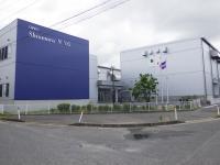 植え込みの横に建っている紫色と白の外壁の真丸特殊紙業株式会社の建物の外観写真