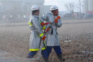 田んぼに向かって放水する2名の消防団員の写真