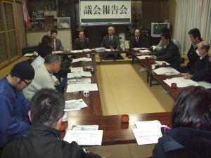 熊居会館で輪になって座り議会報告会を行っている男性たちの写真